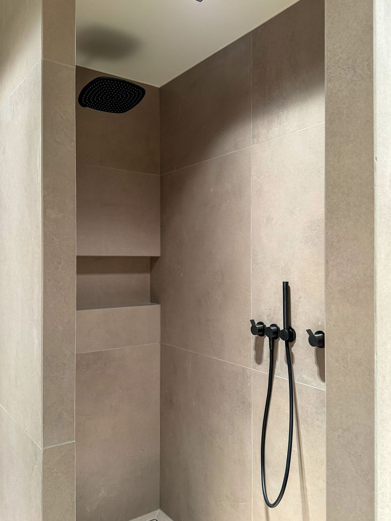 Dusche in hellem Naturstein mit schwarzer Armatur