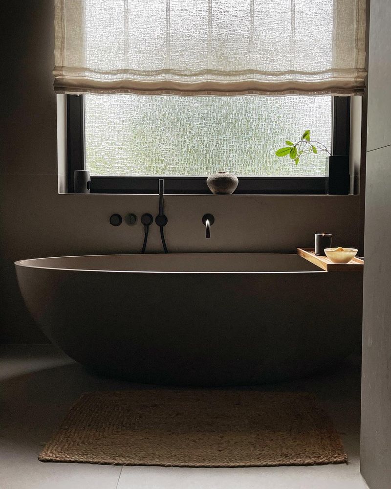 Freistehende Badewanne vor einem Fenster mit Leinenrollo